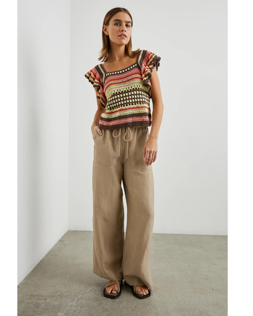  An image of a woman in a full-body pose wearing the Anna Crochet Top in vibrant tropical colors, paired with loose-fitting beige drawstring pants and black sandals.
