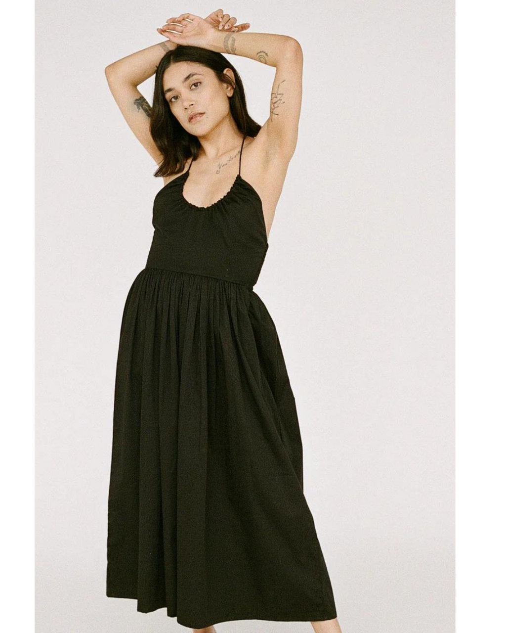 Front side view of the woman, highlighting the soft organic poplin fabric and mid-length design of the Halter Midi Dress in Black.