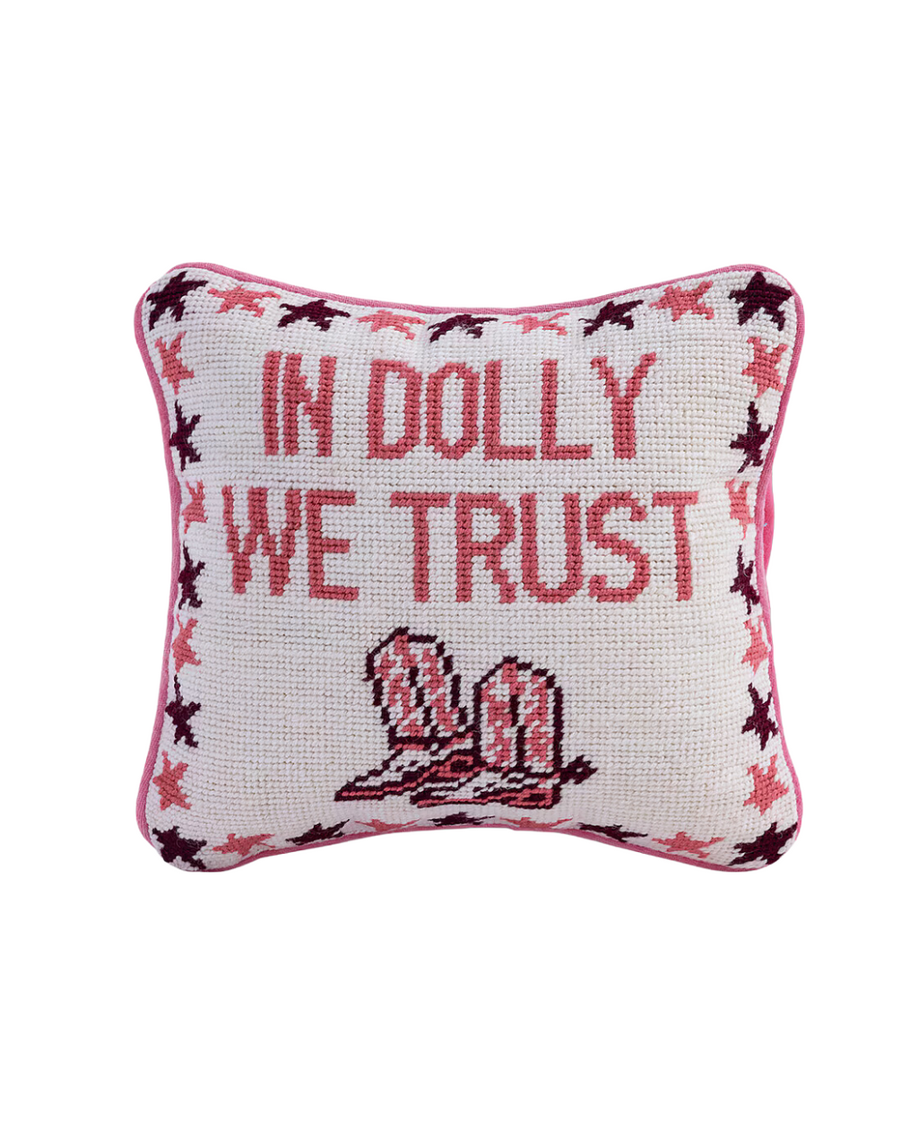 A square needlepoint pillow with a pink border and a pattern of stars in varying shades of pink and burgundy along the edges. The center of the pillow features the text "IN DOLLY WE TRUST" in pink needlepoint, above an image of pink cowboy boots.