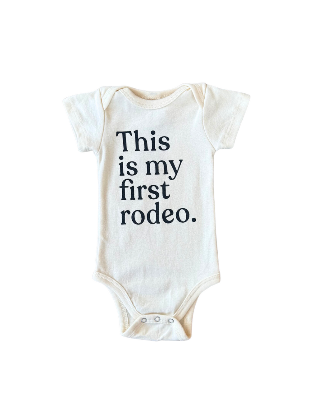 A cream-colored baby onesie with short sleeves and the text "This is my first rodeo." printed in black on the front, displayed against a white background.