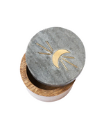 Image of a round moon box with a lid featuring a moon and rays design in brass, made of black marble and mango wood. 