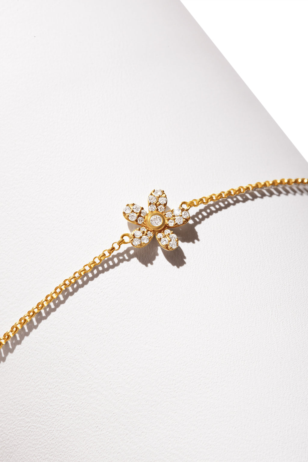 A gold bravelet featuring a dainty flower-shaped charm encrusted with diamonds. 