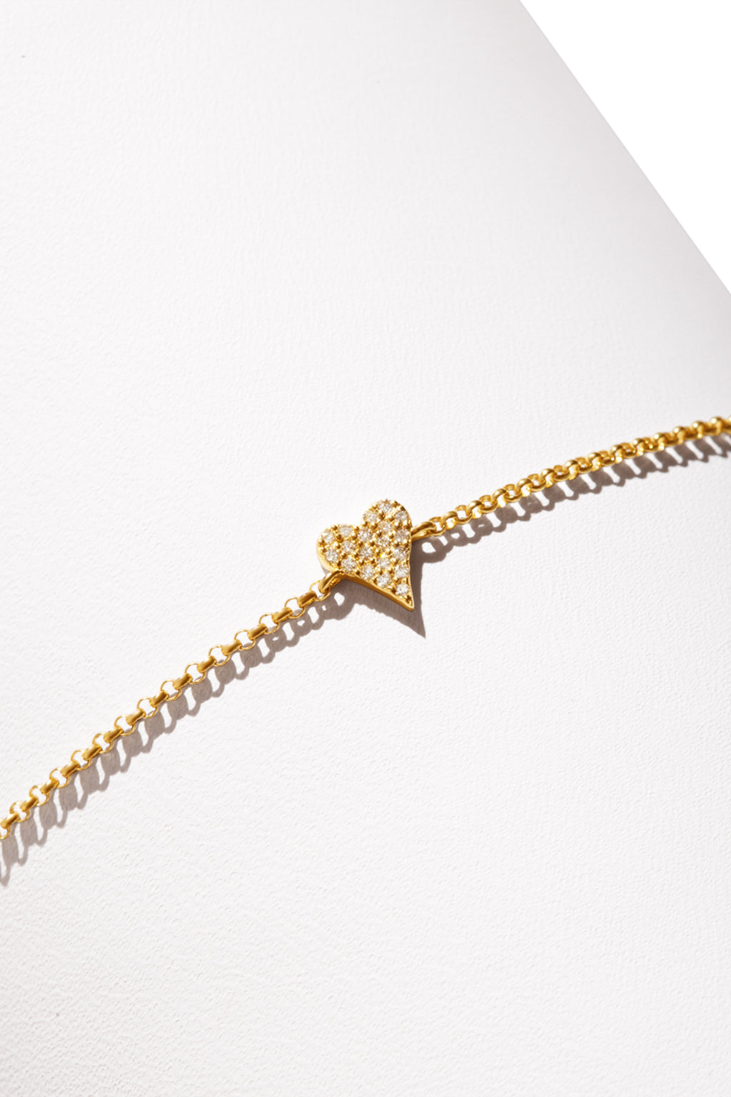 A 14k gold bracelet featuring a heart-shaped charm encrusted with diamonds. 