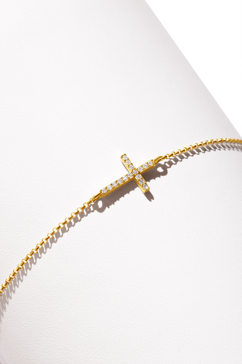 A 14k gold bracelet featuring a cross-shaped charm encrusted with a sparkling diamonds. 