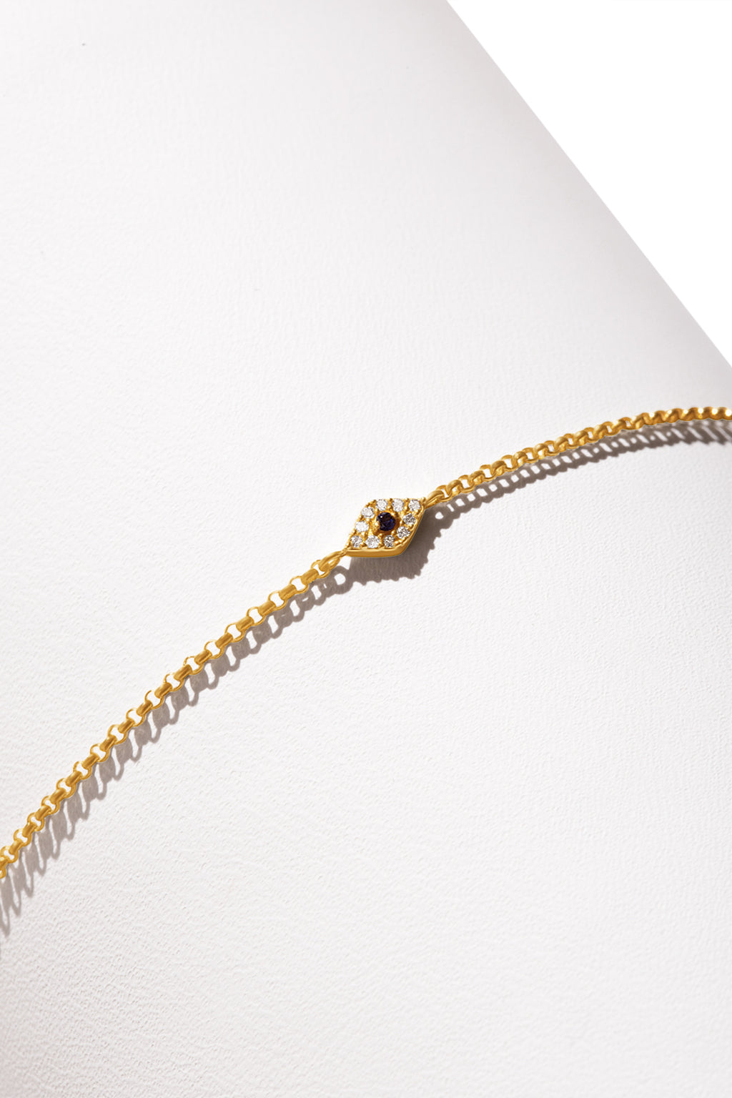 A 14K gold bracelet featuring a small diamond-shaped charm encrusted with diamonds and a central dark gemstone. 