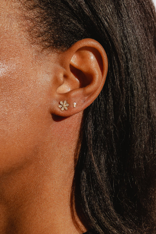 A close-up of a women's ear wearing a gold daisy-shaped stud earring encrusted with diamonds. 