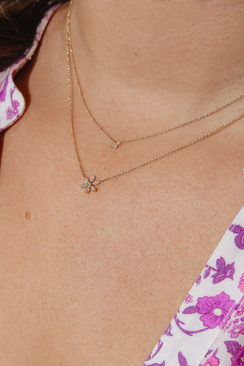 A close-up of a woman's neck wearing two delicate gold necklaces, one with a small diamond - encrusted daisy pendant and the other with a tiny butterfly pendant. 